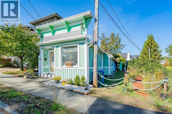 Side view of a small green residential building with white trim and a fenced yard. - 660 Albert St, Nanaimo