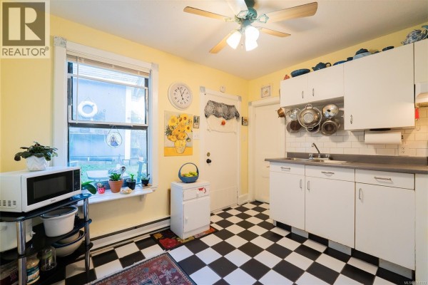 Kitchen with white cabinets, a microwave, a window, and a black and white checkered floor. - 660 Albert St, Nanaimo
