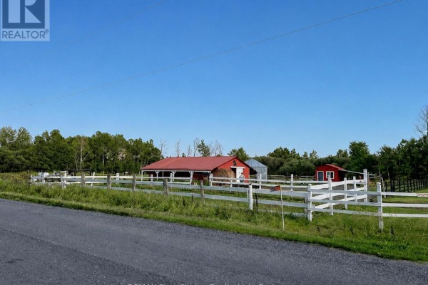 View of the property from the road, featuring white fences, red barns, and mature trees. - 661 Stewart Road, Alberton