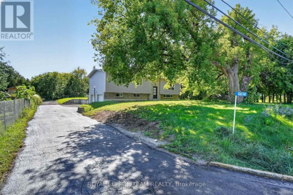 Driveway leading to the property at 6614 Parkway Road, Ottawa, with a green lawn and trees. - 6614 Parkway Road, Ottawa