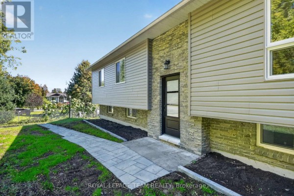 Close-up of the front entrance with a grey stone facade, dark door, and paved walkway. - 6614 Parkway Road, Ottawa