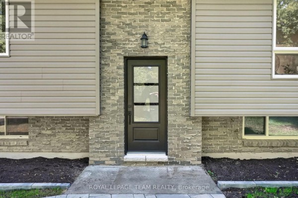 Front door of the house, a dark metal door with glass panels, set against grey stone. - 6614 Parkway Road, Ottawa