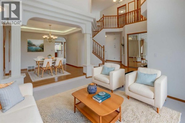 Living room with two white armchairs, a coffee table, and a view of the dining room. - 662 Arbour Lake Drive Nw, Calgary