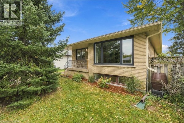 Close-up of the front exterior of a yellow brick bungalow with foliage. - 662 Dynes Road, Burlington