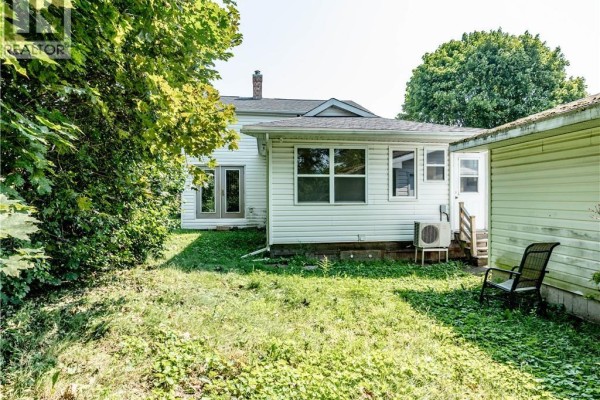 Rear exterior of the house with a small green lawn and dense trees. - 662 Evangeline, Dieppe