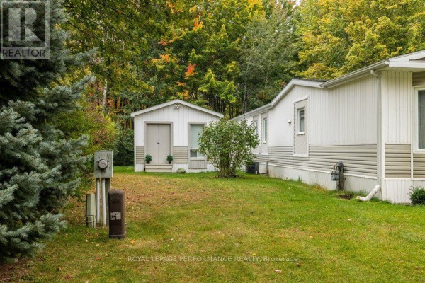 Rear view of the manufactured home and detached shed surrounded by grass and trees. - 6636 Vista Patrick Private, Ottawa