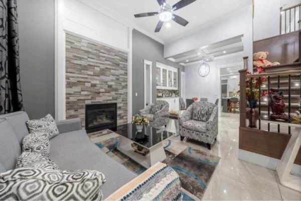 Living room featuring a grey sofa, stone fireplace, patterned armchairs, and a glass coffee table. - 6637 121a Street, Surrey