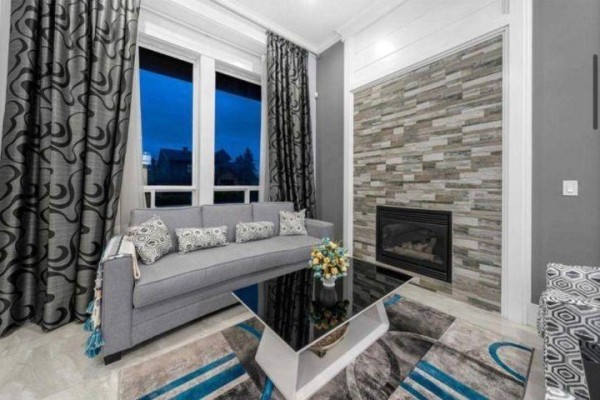 Grey sofa and stone fireplace in a living area with patterned curtains and a glass coffee table. - 6637 121a Street, Surrey