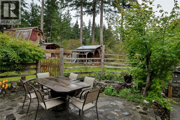 Outdoor patio with a wooden table and chairs, a rustic fence, and surrounding greenery. - 665 Fox Rd, Quadra Island