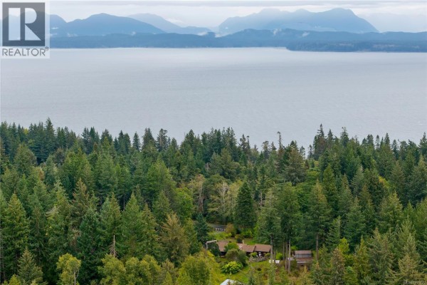 Panoramic view from above, showing the house nestled in a dense forest overlooking a wide body of water. - 665 Fox Rd, Quadra Island