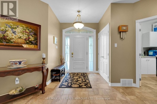 The house's entryway with beige walls, tile flooring, a dark floral rug, a console table, and white double doors. - 6662 Sutherland Avenue, South Glengarry