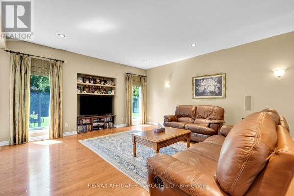 A spacious living room with tan walls, a large area rug, leather couches, a TV console, and hardwood floors. - 6662 Sutherland Avenue, South Glengarry