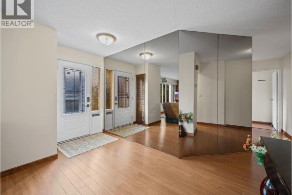 Interior foyer with light wood laminate flooring, mirrored walls, and two front doors. - 667 Cypress Street, Coquitlam