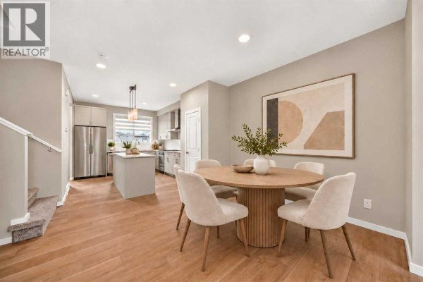 Dining area with round wooden table, chairs, and open view to kitchen and stairs. - 668 Savanna Drive Ne, Calgary