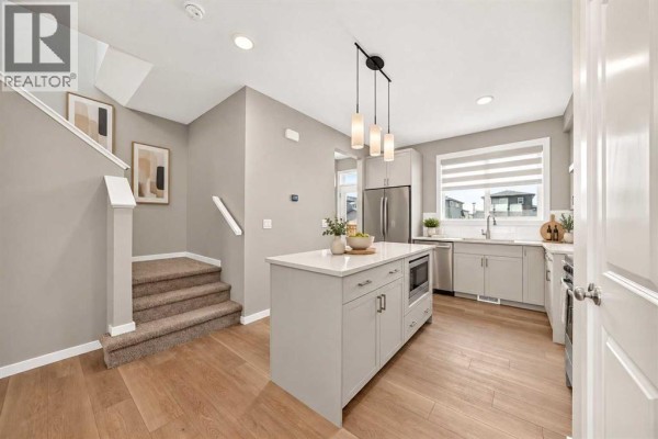 Kitchen with island, stainless steel appliances, light grey cabinets, and stairs leading up. - 668 Savanna Drive Ne, Calgary
