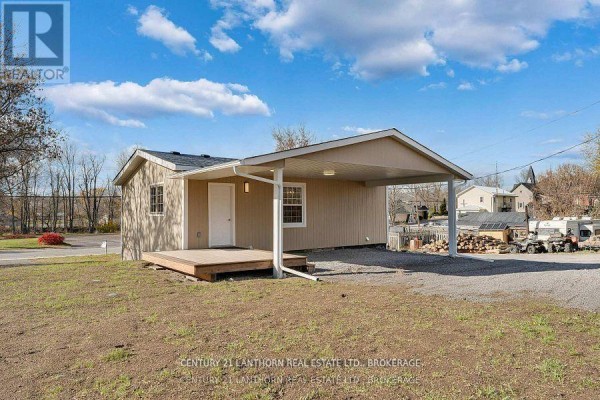 Small building with beige siding, a covered carport, and a wooden deck. - 6682 Wheeler Street S, Stone Mills