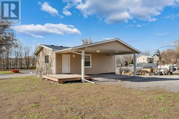 Side view of a single-story structure with beige siding and a covered carport. - 6682 Wheeler Street, Stone Mills