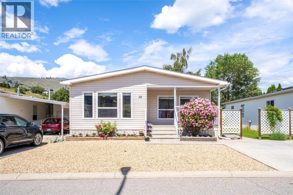Single-story mobile home with beige siding, white trim, and a covered front porch. - 6688 Tronson Road Unit# 38, Vernon