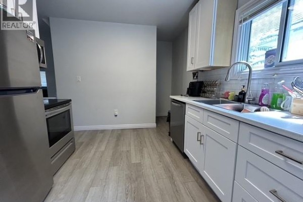 Kitchen view showing stainless steel refrigerator, stove, white cabinets, and light wood-look flooring. - 669 Bridge Avenue, Windsor