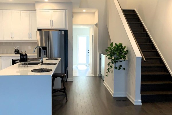A bright open-concept kitchen with white cabinets, stainless steel appliances, and a dark wood staircase. - 669 Honeydew Street, Ottawa
