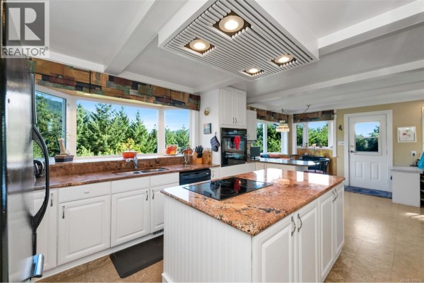 Kitchen with white cabinets, granite countertops, an island with a cooktop, and bay windows. - 6693 Genoa Bay Rd, Duncan