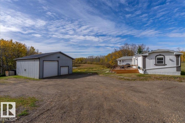 Exterior view of a large grey metal outbuilding with two garage doors, set on a gravel pad with surrounding trees. - 67 50514 Range Road 202, Rural Beaver County