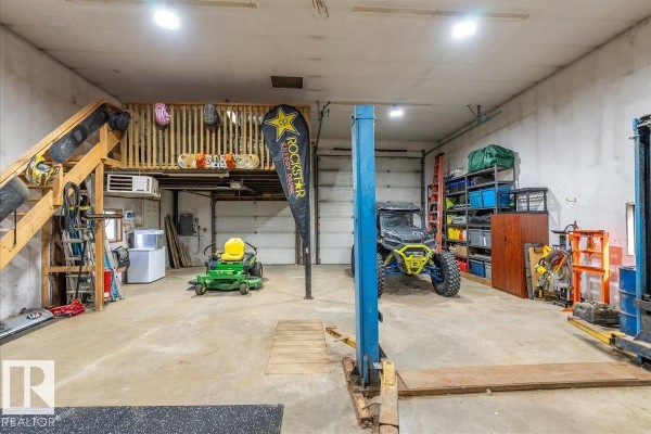 Interior view of a large workshop space with a loft, wooden stairs, garage doors, a tractor, and weightlifting equipment. - 67 50514 Range Road 202, Rural Beaver County