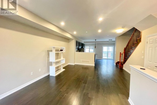 Open concept living area with dark hardwood floors, beige walls, white shelving unit, and staircase. - 67 Antibes Drive, Toronto