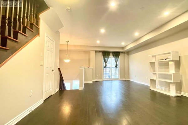 Living room with dark hardwood floors, beige walls, white shelving unit, and view of kitchen and balcony. - 67 Antibes Drive, Toronto