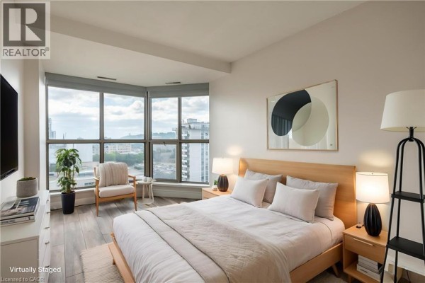 Modern bedroom with large bay window city view, queen bed, and accent chair - 67 Caroline Street S Unit# 13a Hamilton