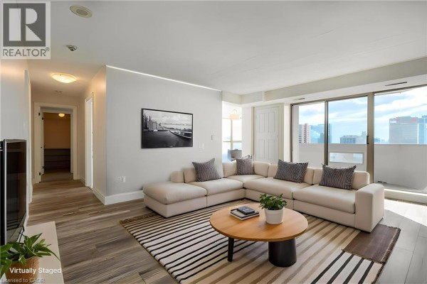 Living room with sectional sofa, coffee table, striped rug, and city view - 67 Caroline Street S Unit# 13a Hamilton
