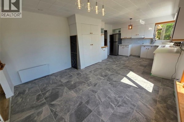 Kitchen and dining area with white cabinets, grey tiled floors, and large windows. - 67 Narcisse-beaulieu Street, Edmundston