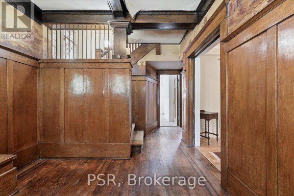 Interior hallway with rich wood paneling, a wooden staircase with spindles, and hardwood floors. - 67 Oakwood Avenue, Toronto
