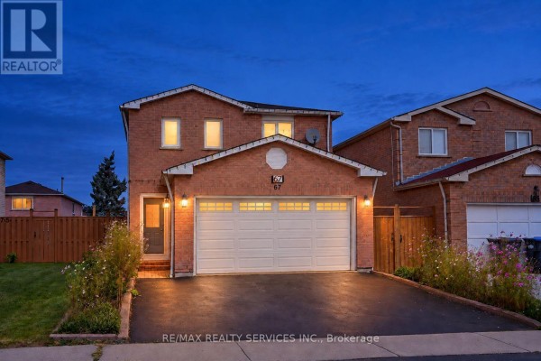 Front exterior view of a two-story brick house with a white garage door and driveway at dusk. - 67 Sandmere Avenue, Brampton