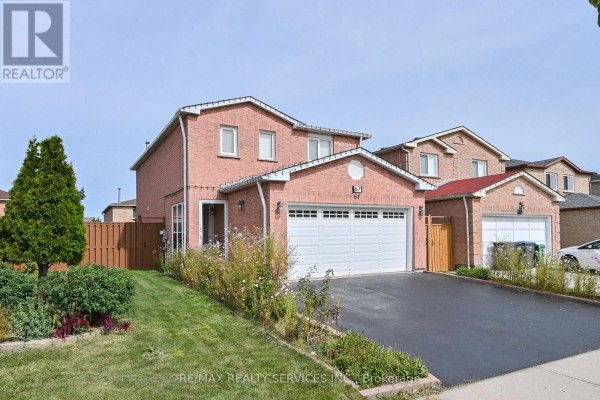 Side exterior view of a two-story brick house with a green lawn and a wooden fence. - 67 Sandmere Avenue, Brampton
