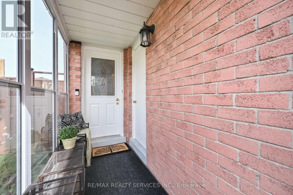 Covered entryway with brick wall, white door, dark mat, and seating area. - 67 Sandmere Avenue, Brampton
