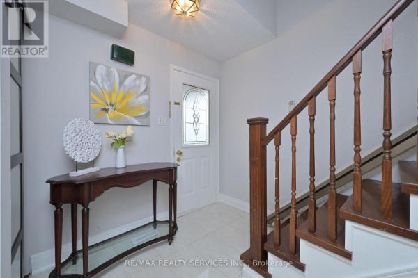 Foyer with a console table, artwork, and a wooden staircase with white risers. - 67 Sandmere Avenue, Brampton