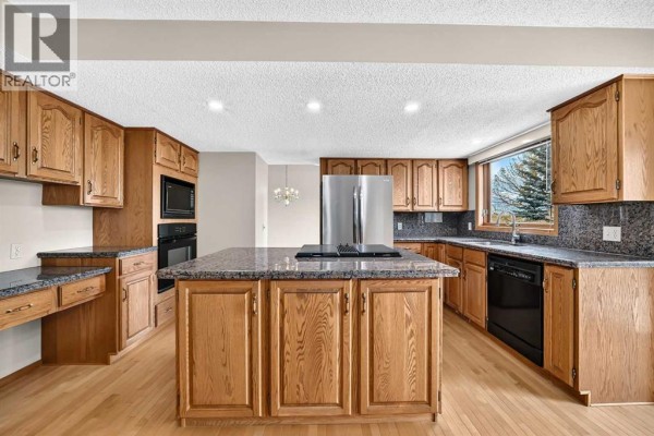Spacious kitchen with light wood cabinets, granite countertops, and stainless steel appliances. - 67 Suncanyon Park Se, Calgary