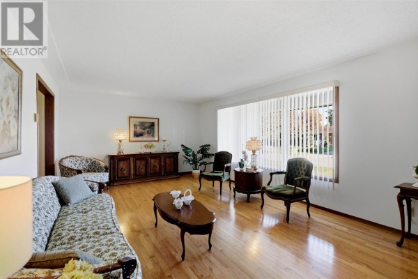 Living room with white walls, hardwood floors, floral sofa, and a large window. - 67 Westridge Rd, Sault Ste  Marie