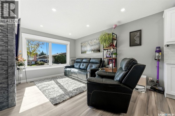 Living room with grey walls, a black leather sofa, recliner, grey rug, and large window. - 6702 Whelan Drive, Regina