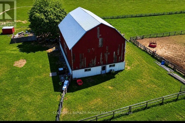 Aerial view of a large red barn with a white metal roof, surrounded by green fields and paddocks. - 6703 Pine Plains Road E, Adjala Tosorontio