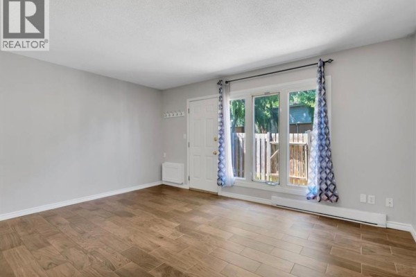 Living room with wood laminate flooring and a large window with blue patterned curtains. - 6732 Roseville Garden Drive, Windsor