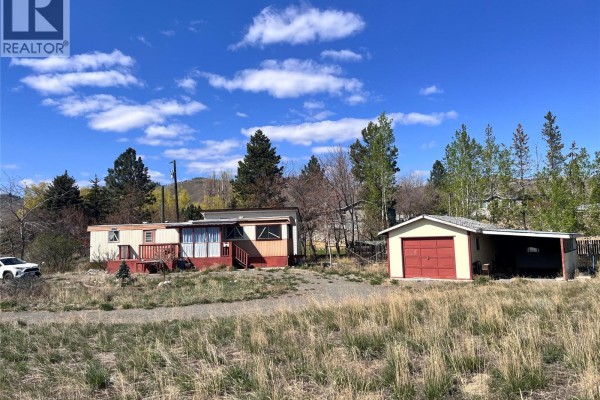 Exterior view of a mobile home with a red-trimmed porch and a detached garage with a red door. - 6736 Pinecrest Drive, Kamloops