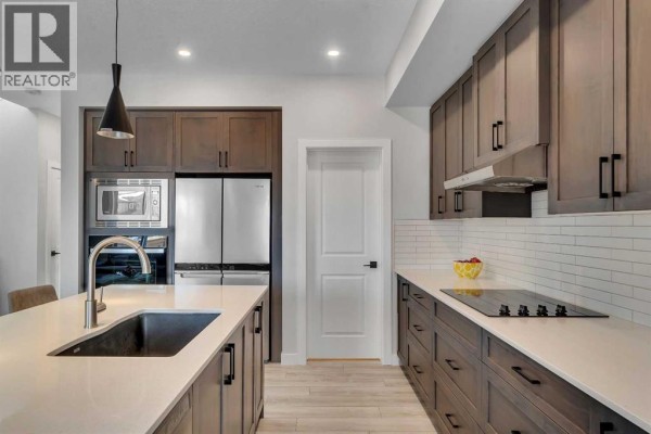 Kitchen with dark brown cabinets, white countertops, and an island with three stools, adjacent to a dining area. - 674 Creekmill Court Sw, Airdrie