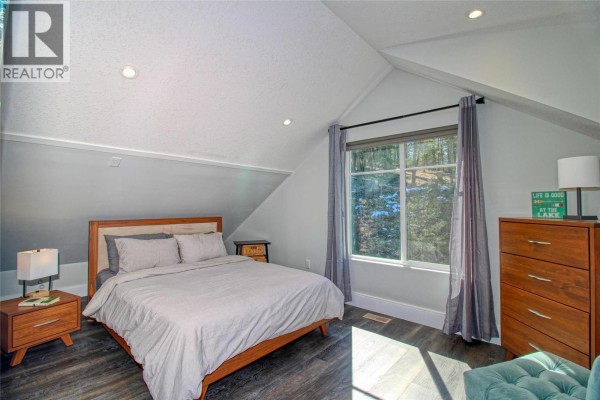 Bedroom with a queen-size bed, vaulted ceiling, and a large window with wooded views. - 6742 Marbella Loop Unit# 302, Kelowna