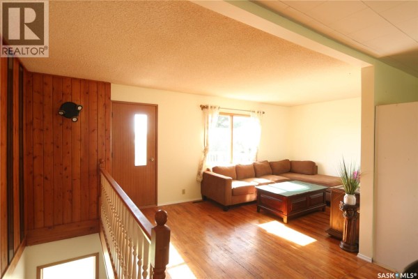 Living room with wood paneling on the left, a door to the exterior, a large brown sectional, and hardwood floors. - 675 Fort San Road, Fort San