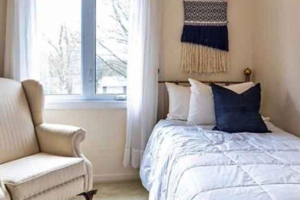 Bedroom with a twin bed, armchair, and a window with white curtains. - 675 Waverly Street N, Oshawa
