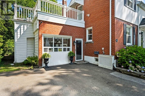 Side view of the house showing a detached garage door, red brick, and a white balcony railing. - 6751 Barker Street, Niagara Falls
