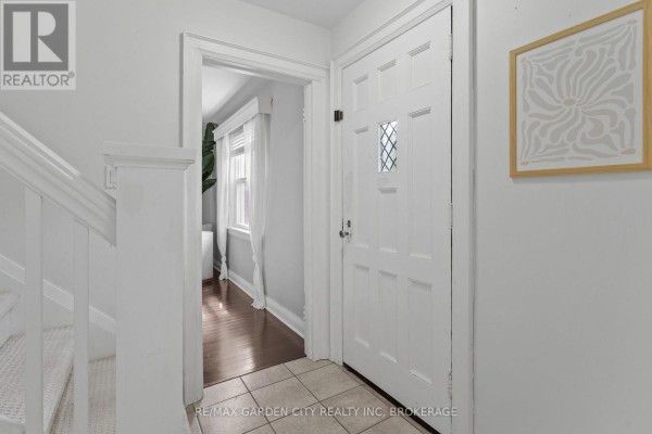 Interior view of a white entryway with a closed white door, carpeted stairs, and a framed picture. - 6751 Barker Street, Niagara Falls