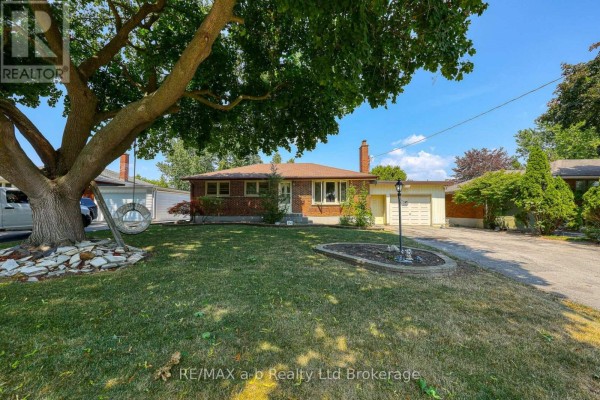 Front yard view of a brick bungalow with a large mature tree and grass lawn. - 6752 Beattie Street, London South